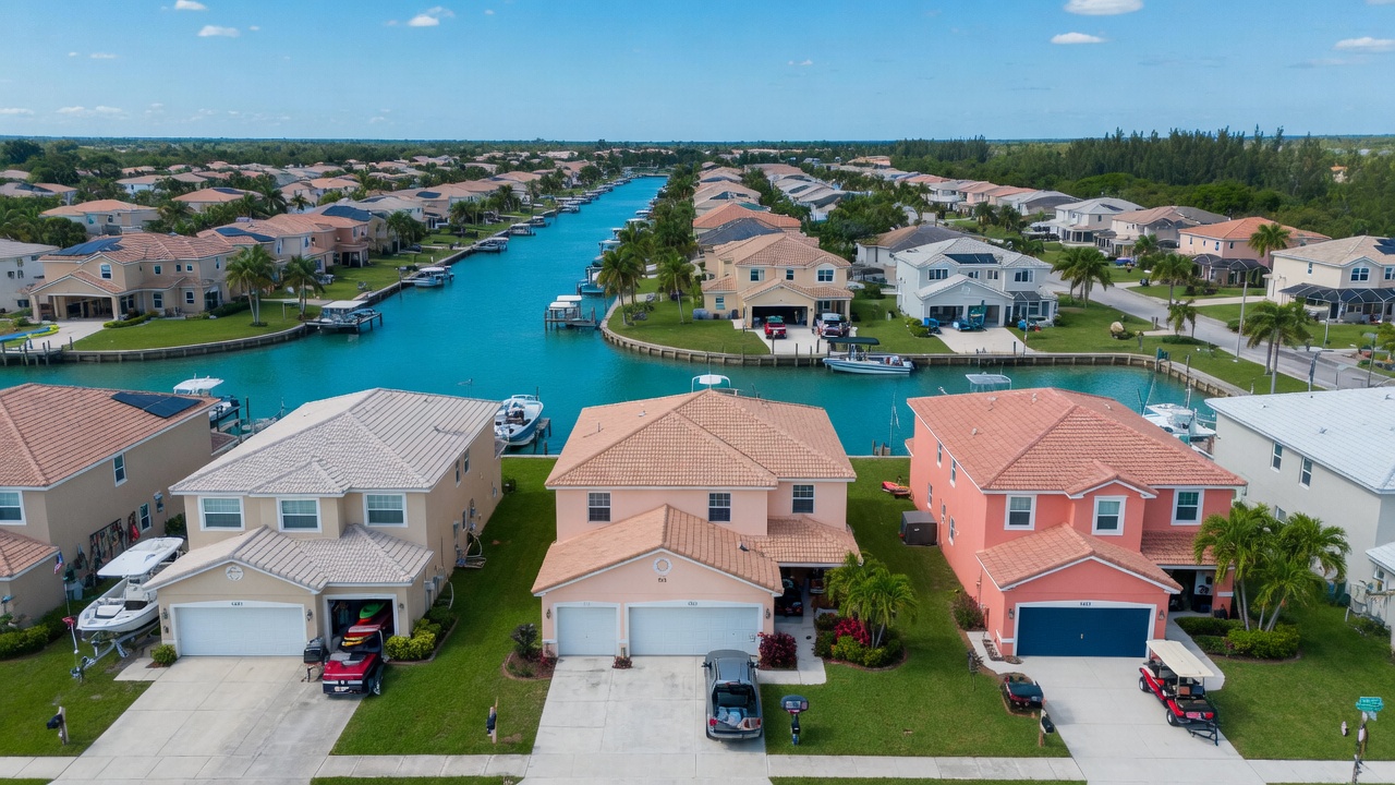 Aerial view of Cape Coral Florida waterfront community with focus on several homes with garage doors, highlighting 33904 area, bright clear day, 8K drone photography style
